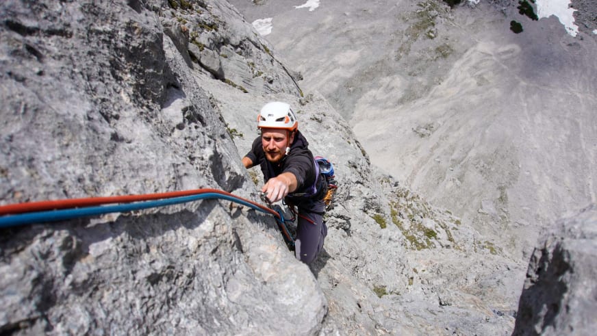Bergführer Jakob Fink klettert in weißem Helm und Klettergurt an grauer Kalksteinwand mit rot-blauem Seil.
