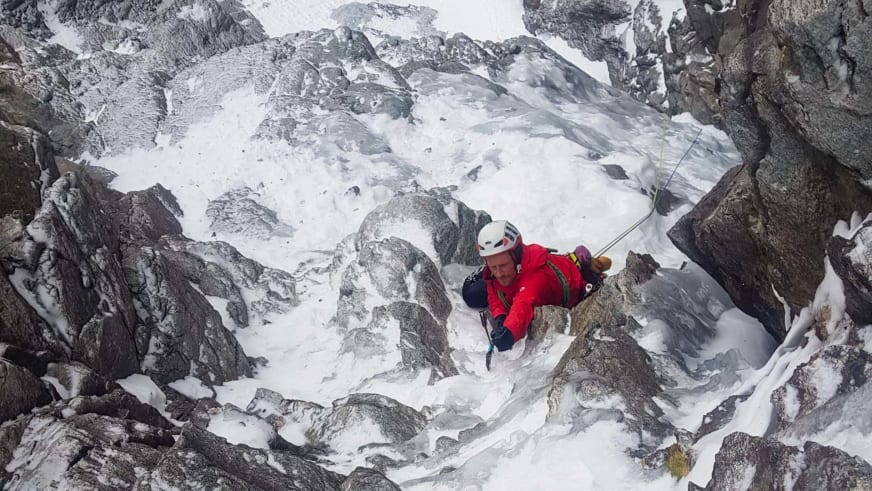 Jakob Fink klettert als Bergführer in roter Winterjacke und weißem Helm an vereister Felswand zwischen Schnee.