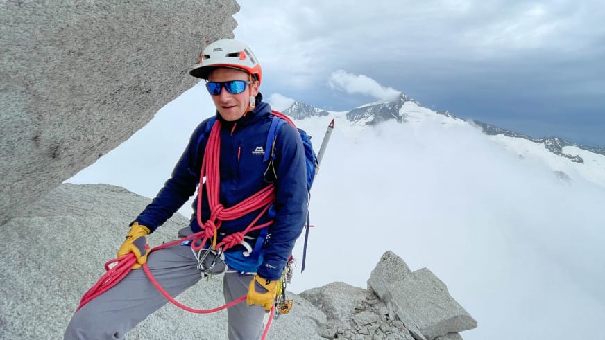 Bergführer Jakob Fink steht mit weißem Helm und blauer Sonnenbrille auf verschneitem Felsgrat mit rotem Seil.