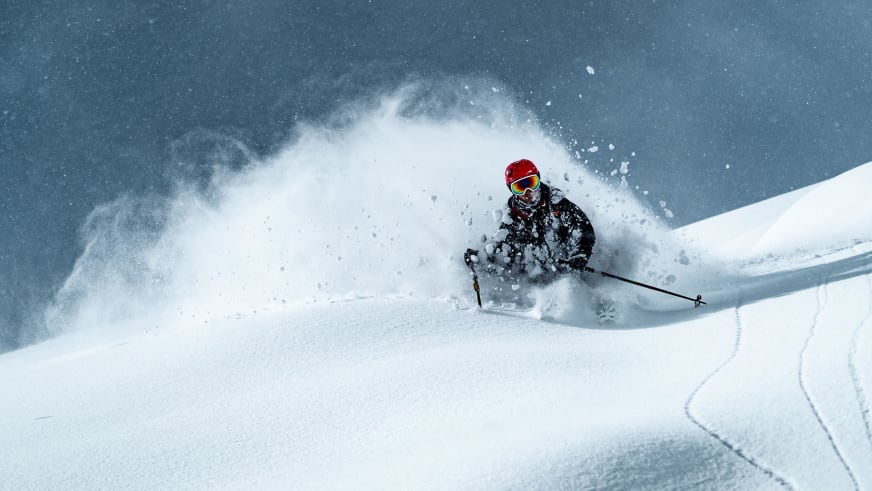 Bergführer Jakob Fink fährt mit Skiern durch tiefen Pulverschnee und wirbelt dabei eine große Schneewolke auf.