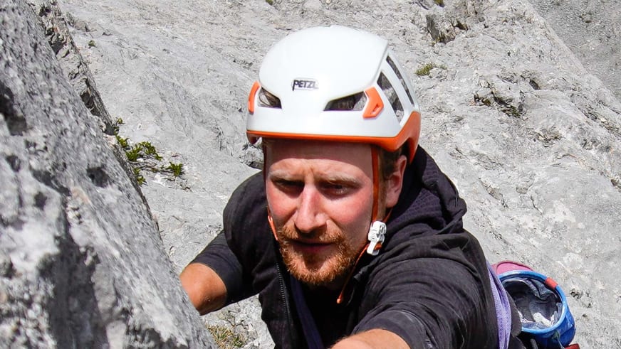 Jakob Fink trägt als Bergführer weißen Petzl Helm mit orangen Elementen vor hellem Kalkgestein im Hintergrund.