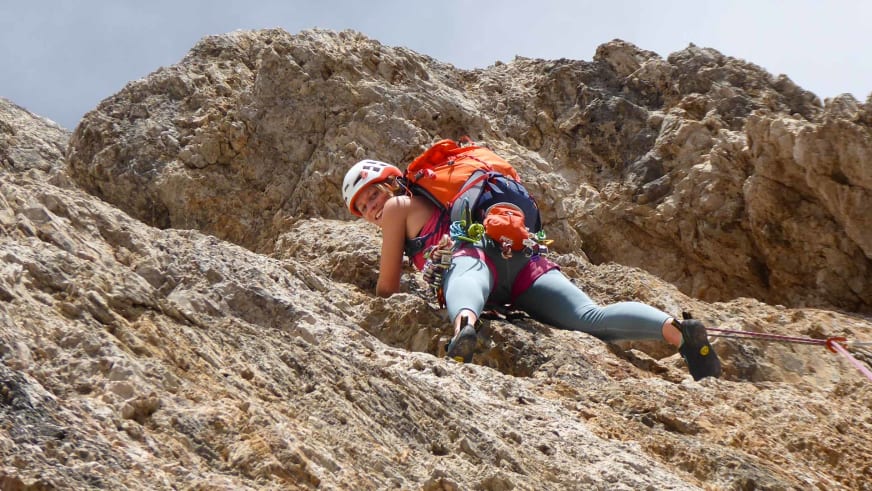 An steiler Kalksteinwand klettert Bergwanderführerin Anna Biller mit rotem Helm und Kletterausrüstung am Klettergurt.
