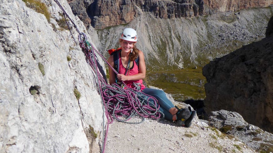 Auf Felsvorsprung pausiert Bergwanderführerin Anna Biller beim Klettern und hält ein pink-graues Kletterseil in den Händen.