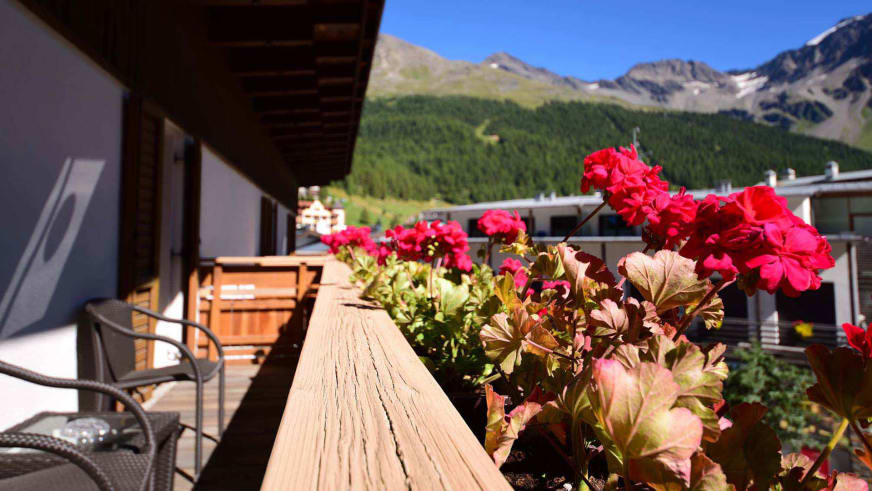 Balkon mit roten Geranien im Alpin Garni die kleine Post bietet Panoramablick auf verschneite Berggipfel.