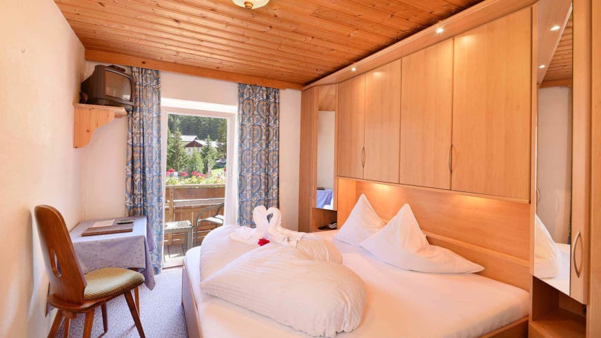 Gemütliches Doppelzimmer im Alpin Garni die kleine Post mit Holzmöbeln und Balkonblick ins Grüne.