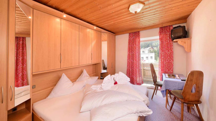 Doppelzimmer im Alpin Garni die kleine Post mit Holzmöbeln, roter Dekoration und Blick zum Balkon.