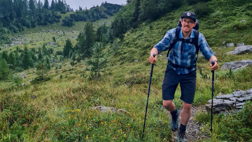 Bergwanderführer Timo Reichert steigt mit Wanderstöcken einen grasbewachsenen Bergpfad in karierter Jacke hinauf.