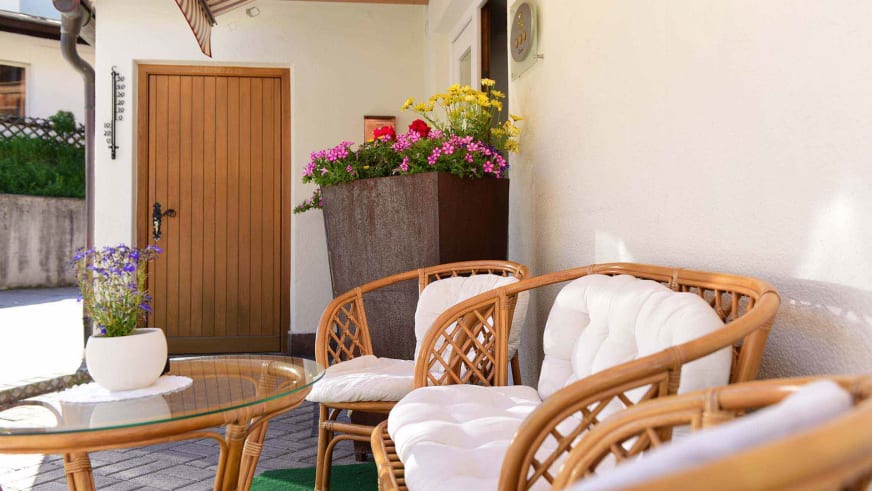 Gemütliche Terrasse mit Rattanmöbeln im Alpin Garni die kleine Post unter Holzdach mit Blumenschmuck.