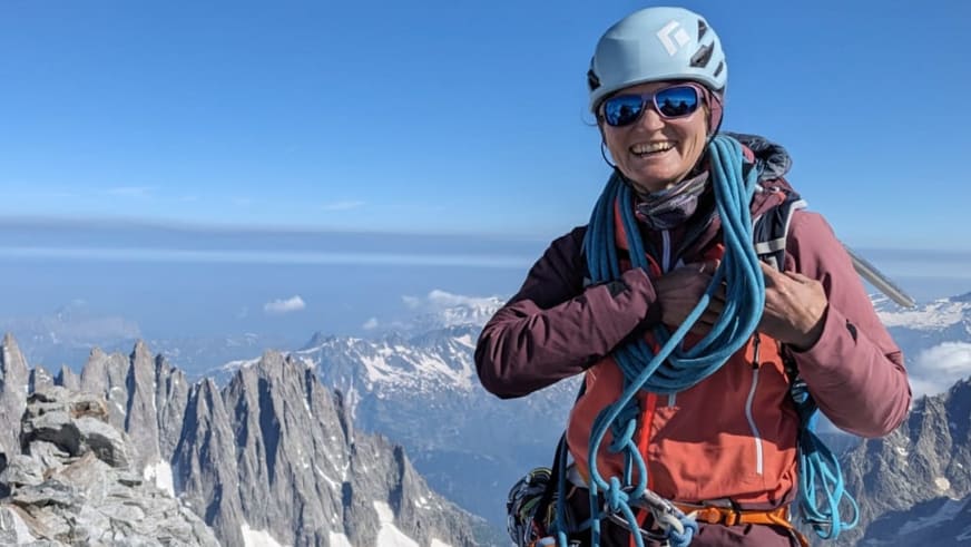 Portrait der lächelnden Bergführerin Elisabeth Seibt mit weißem Helm und Kletterausrüstung vor einem Panorama aus Kalksteinbergen.