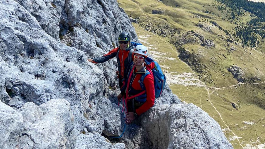 Bergführer Alexander Reisenhofer klettert mit Partner an steiler Kalksteinwand über grünen Almhängen.