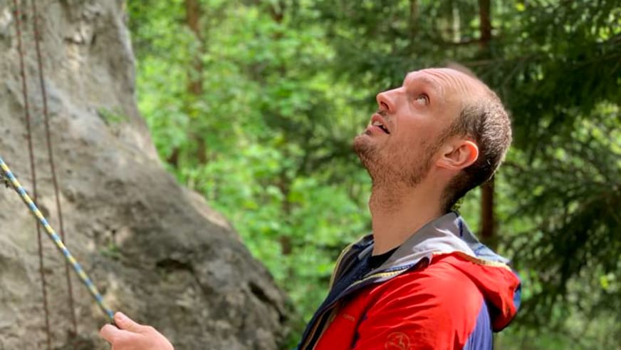 Mit roter Funktionsjacke blickt Bergführer Alexander Reisenhofer nach oben und hält ein Kletterseil.