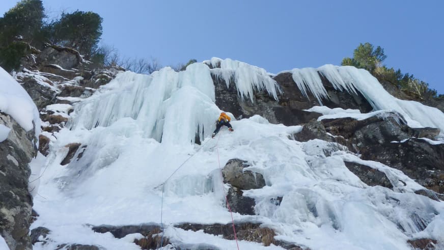 Bergführer Alexander Reisenhofer klettert mit Eisgeräten an vereister Felswand mit dicken Eiszapfen.