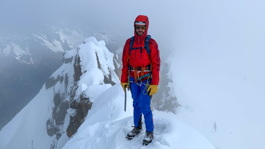 Bergführer Tim Lenz steht in roter Jacke mit Steigeisen und Eispickel auf schneebedecktem Grat.