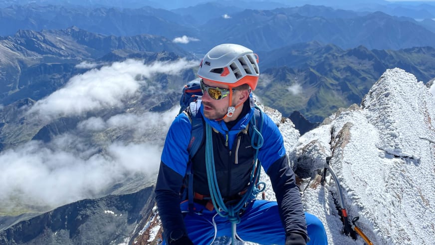 Bergführer Tim Lenz sitzt in blauer Softshell-Kleidung mit weißem Helm auf hellem Kalkfels.