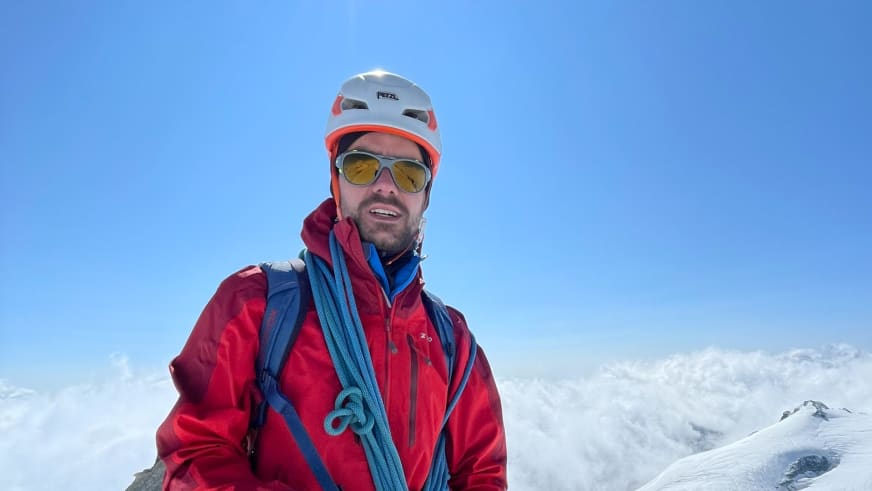 Bergführer Tim Lenz trägt weißen Helm und Gletscherbrille vor verschneiter Hochgebirgslandschaft.
