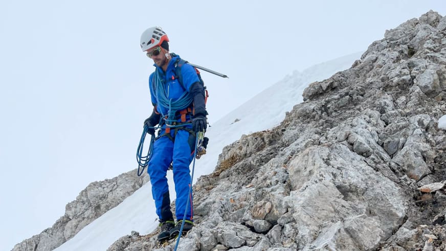 Bergführer Tim Lenz steht in blauer Kleidung mit weißem Helm auf steilem Kalksteinhang.