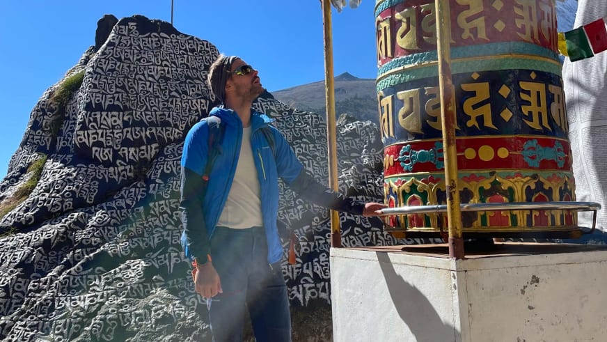 Bergführer Tim Lenz berührt in blauer Jacke ein buddhistisches Gebetsrad mit tibetischen Schriftzeichen.