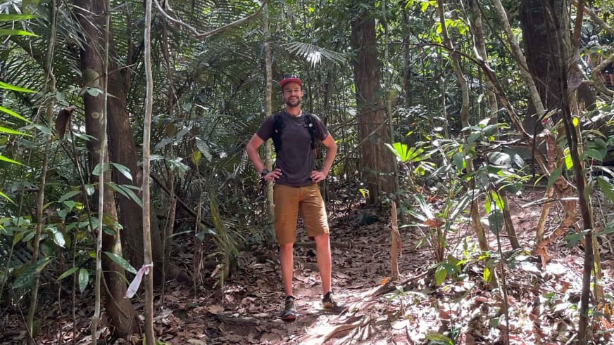 Bergführer Tim Lenz steht lächelnd in roter Kappe auf einem Waldweg zwischen tropischer Vegetation.