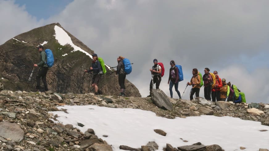 Etwa 15 Bergwanderer folgen Bergwanderführer Tobias Storz über steiniges Gelände mit Schneefeldern im Hochgebirge.
