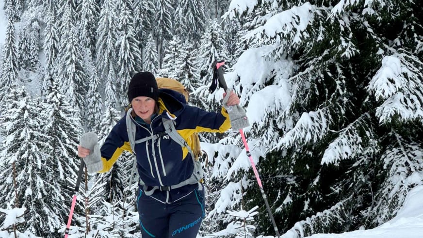 Bergwanderführerin Anna Schärtel bewegt sich mit Schneeschuhen und rosa Stöcken durch verschneiten Nadelwald.