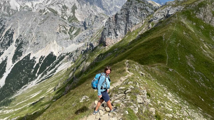 Bergwanderführerin Anna Schärtel wandert auf steinigem Bergweg entlang eines grünen Grats vor schroffen Kalksteinbergen.