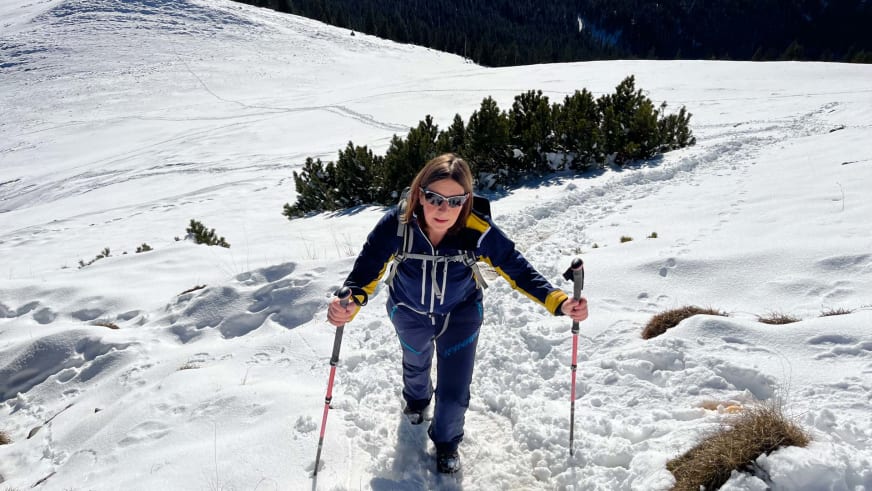 Mit roten Wanderstöcken steigt Bergwanderführerin Anna Schärtel durch tiefen Schnee bergauf in verschneiter Berglandschaft.