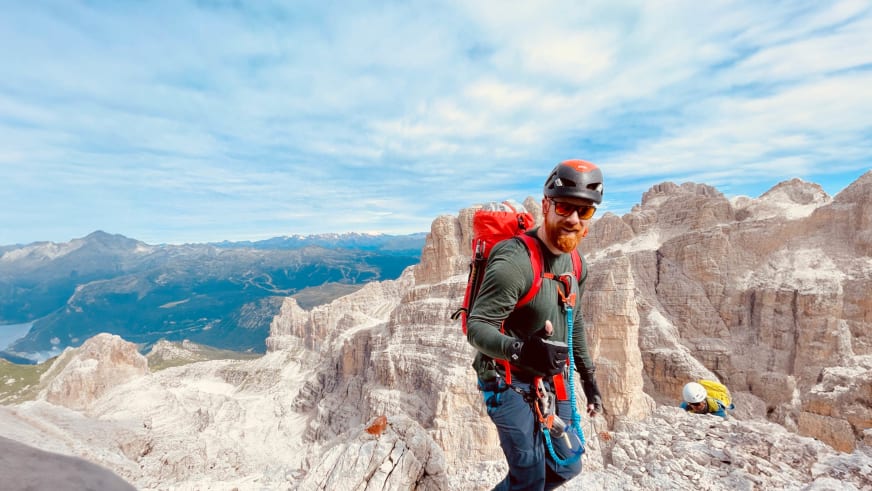 Bergwanderführer Dennis Enders steht mit Kletterausrüstung auf Felsplateau in den Dolomiten mit Panoramablick.