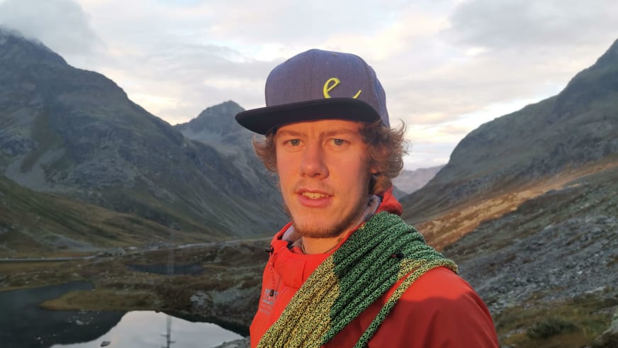 Portrait zeigt Bergführer Florian Storkenmaier mit blauer Schirmmütze und roter Jacke vor Bergpanorama.