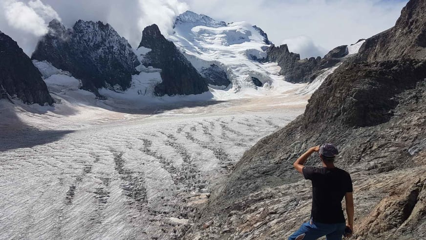 Bergwanderführer Johannes Geipel sitzt auf Felsgestein und blickt auf einen großen Gletscher mit deutlichen Spalten und umgebenden Gipfeln.