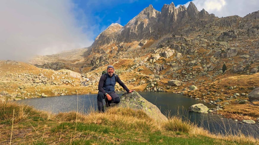 Am Ufer eines Bergsees im Arantal sitzt Bergwanderführer Nacho Carreras Codina auf bemoosten Felsen.