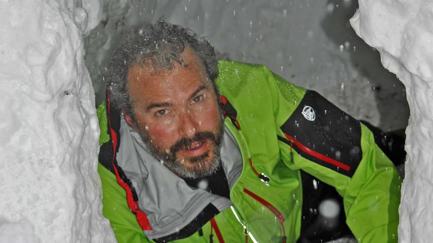 In Schneehöhle sitzt Bergwanderführer Nacho Carreras Codina in grüner Hardshelljacke bei starkem Schneefall.