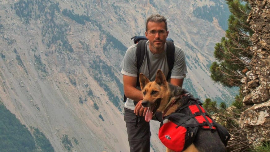 Bergwanderführer Nacho Carreras Codina sitzt mit Schäferhund auf Felsvorsprung vor weiter Berglandschaft der Pyrenäen.