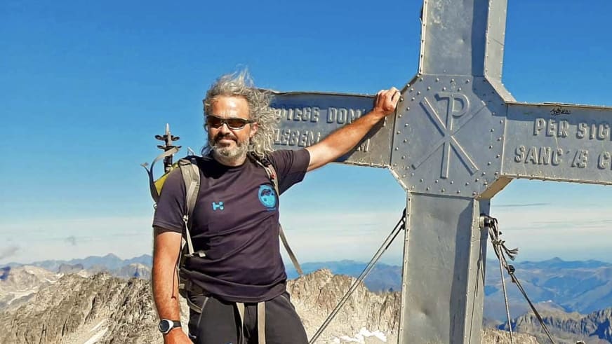 Bergwanderführer Nacho Carreras Codina steht am Gipfelkreuz des Aneto mit Sonnenbrille und Rucksack.