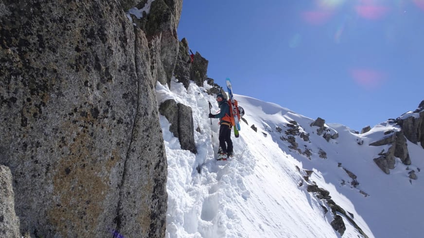 Bergwanderführerin Marie Nimsgern steigt mit Skiern am Rücken über einen verschneiten Felsgrat zwischen steilen Granitwänden auf.