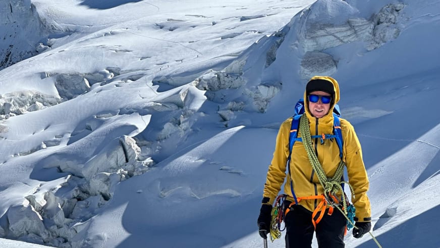 Bergführer Stefan Scheiblauer in gelber Bergjacke mit Eispickel und Kletterausrüstung vor zerklüfteter Gletscherlandschaft.
