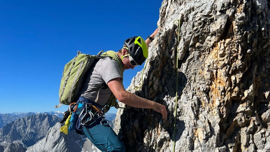 In steiler Kalksteinwand klettert Bergführer Stefan Scheiblauer mit gelbem Helm und Kletterausrüstung bei Sonnenschein.