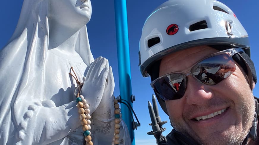 Bergwanderführer Gerald Römpp trägt weißen Kletterhelm und Sonnenbrille, lächelt zwischen weißen Eisformationen vor tiefblauem Himmel.