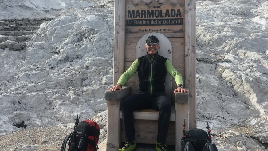 Bergwanderführer Gerald Römpp sitzt entspannt im Holzstuhl vor dem Gipfelschild der Marmolada in den Dolomiten.