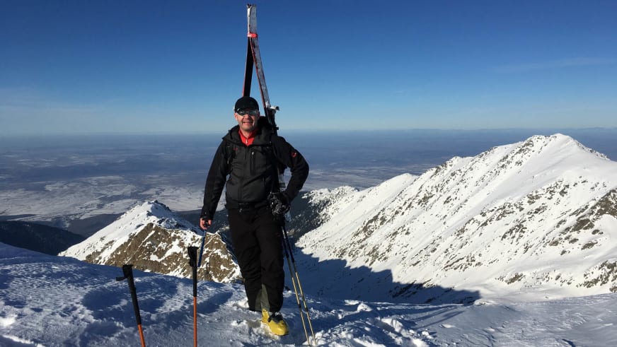 Bergwanderführer Gerald Römpp steht mit Tourenski und Skistöcken auf einem schneebedeckten Berggipfel vor weitem Bergpanorama.