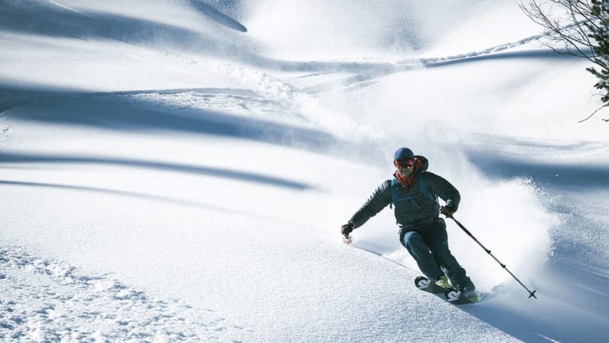 In tiefem Pulverschnee fährt Bergführer Tobias Kostenbader einen steilen Hang ab und wirbelt eine Schneewolke auf.