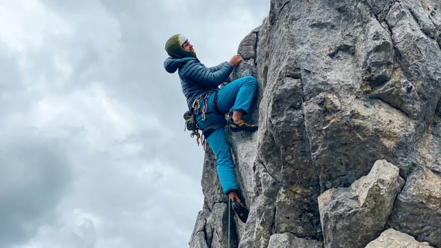 An einer grauen Felswand klettert Bergführer Tobias Kostenbader in blauer Kleidung und grünem Helm mit Klettergurt.
