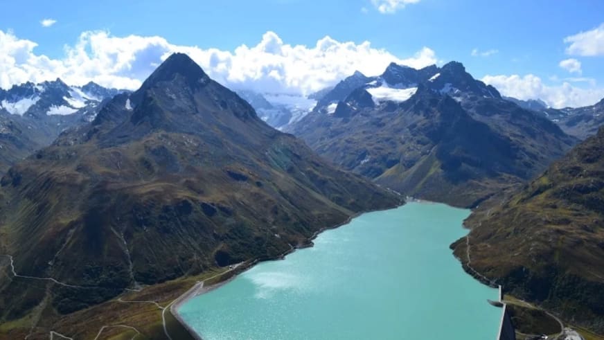 Luftaufnahme des türkisfarbenen Silvretta-Stausees in der Nähe des Berggasthofs Piz Buin mit schneebedeckten Gipfeln.