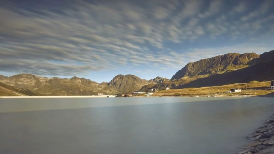 Ruhige Wasserfläche in der Silvretta-Region beim Berggasthof Piz Buin mit Bergkette und goldener Lichtstimmung am Abend.