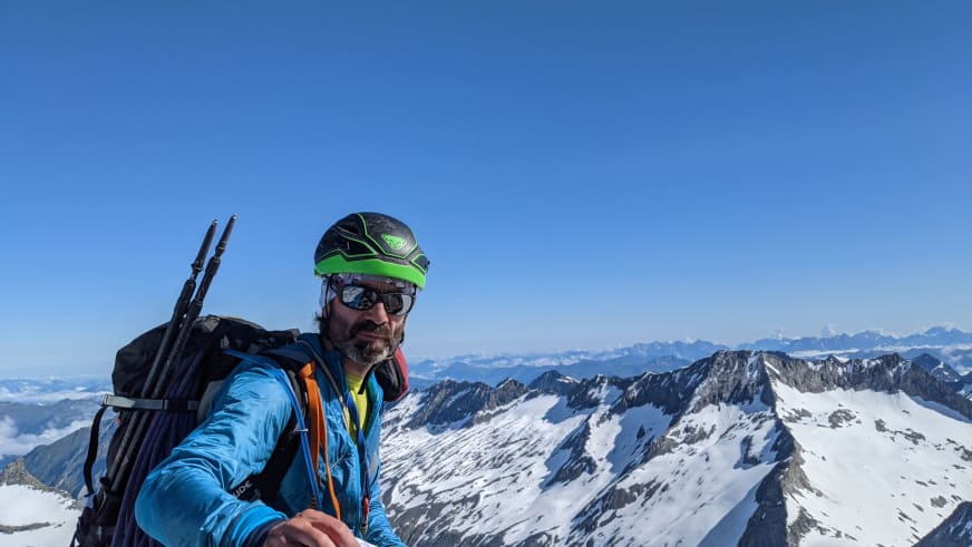 Auf schneebedecktem Gipfel macht Bergwanderführer Karsten Clauß ein Selfie vor Panorama aus schneebedeckten Berggipfeln.
