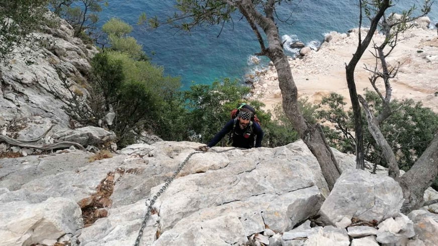 An heller Kalksteinwand klettert Bergwanderführer Karsten Clauß entlang einer Metallkette über türkisblauem Meer.