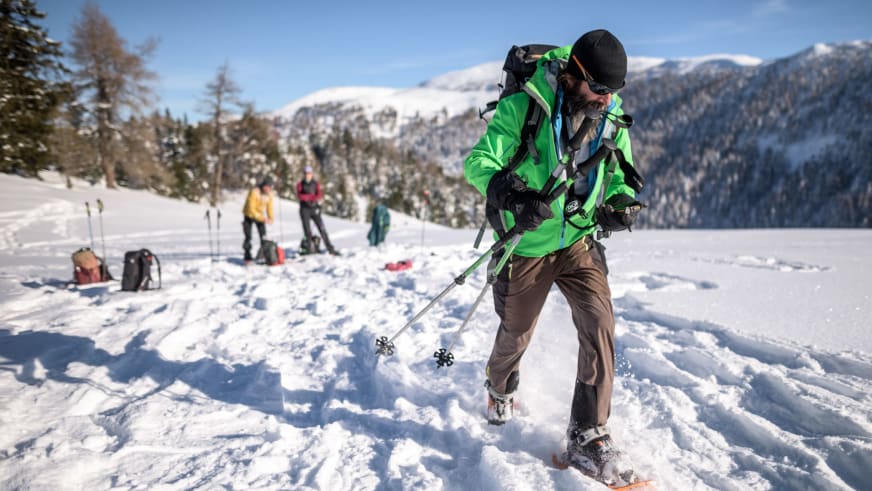 Bergwanderführer Karsten Clauß geht mit Schneeschuhen und grünen Stöcken durch tiefen Pulverschnee auf verschneiter Hochebene.