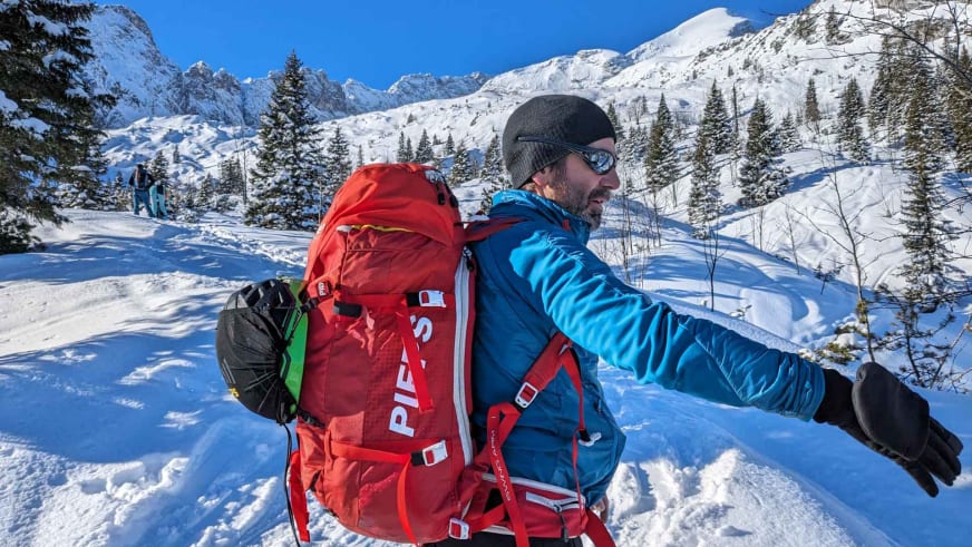 Portrait von Bergwanderführer Karsten Clauß mit rotem Tourenrucksack und blauer Winterjacke in alpiner Winterlandschaft.