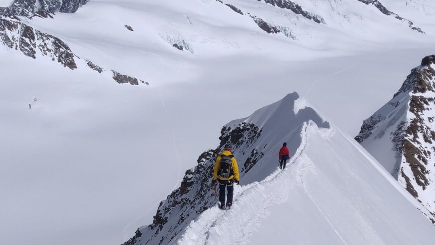 Zwei Personen gehen auf verschneitem Grat durch Neuschnee, Bergführer Alexander Berger führt die Hochtour.