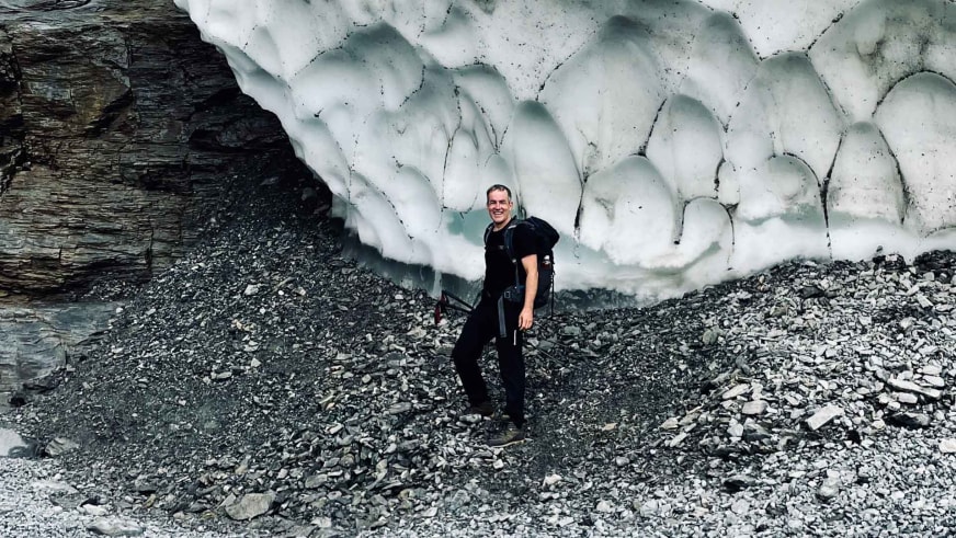 Bergwanderführer Alexander Hoffmann - Kuhnt steht lächelnd vor einer bläulich-weißen Gletscherwand mit Spalten.