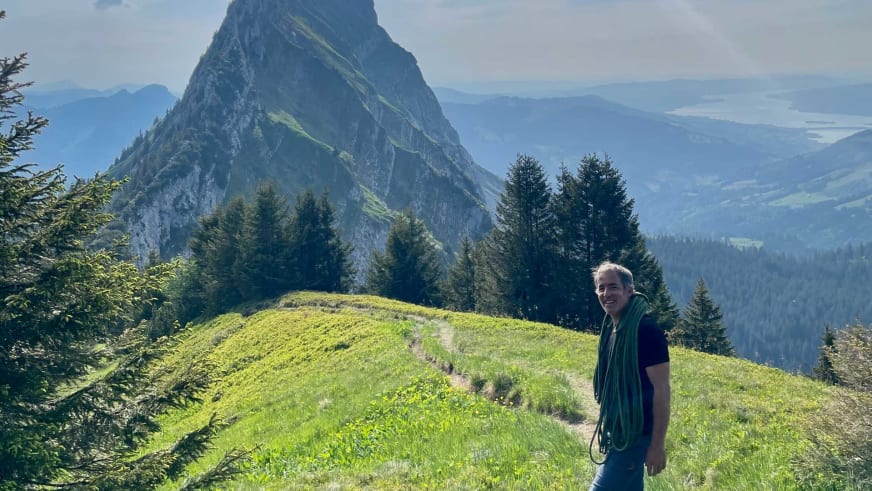 Bergwanderführer Alexander Hoffmann - Kuhnt steht mit grünem Seil auf einem grünen Bergrücken vor einem steilen Felsgipfel.